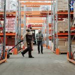 Dois trabalhadores organizam mercadorias em um corredor de armazém.