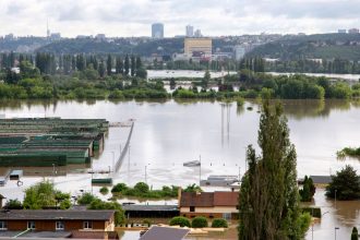 Vista aérea de uma cidade com ruas e construções parcialmente submersas por águas de enchente.