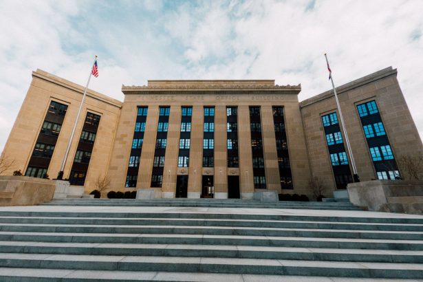 Fachada do Federal Reserve em Washington, vista de baixo, com bandeiras dos Estados Unidos e uma escadaria sob céu nublado.