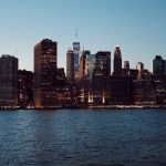Horizonte de Nova York com arranha-céus refletidos na água ao entardecer.
