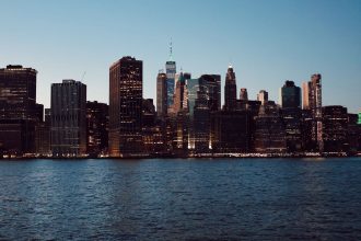 Horizonte de Nova York com arranha-céus refletidos na água ao entardecer.