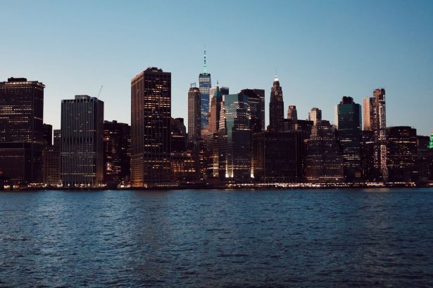 Horizonte de Nova York com arranha-céus refletidos na água ao entardecer.
